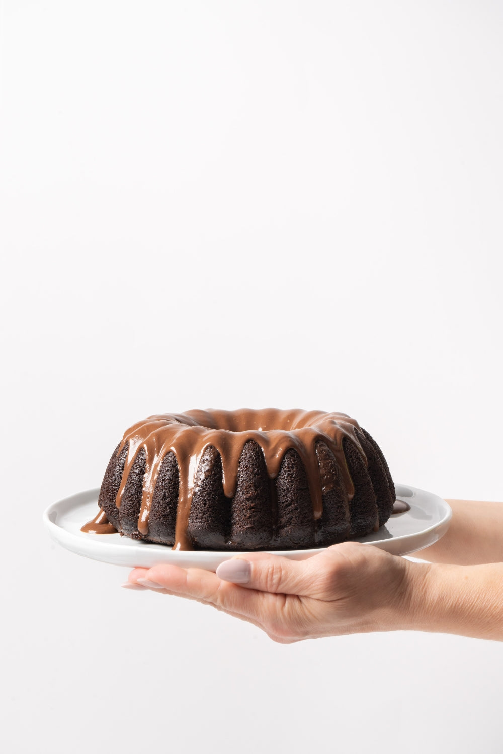 Bundt cake sobre un plato que sujeta un par de manos. 