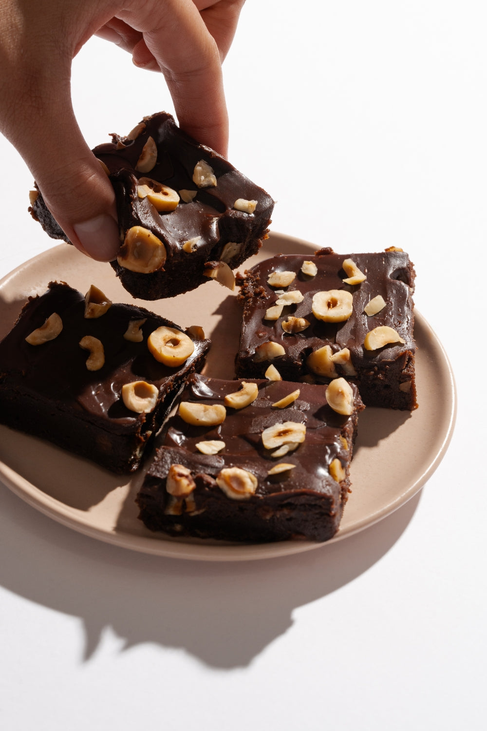 Un plato con cuatro trozos de turrón de choco avellanas. Una mano sujeta un pedazo. 